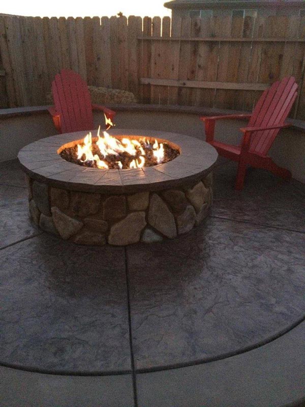 A firepit made of stone sits in a backyard patio.