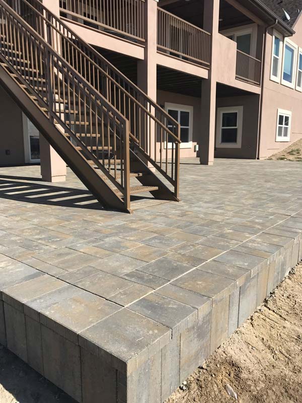 A brick patio with stairs leads up to a house with a brown door.
