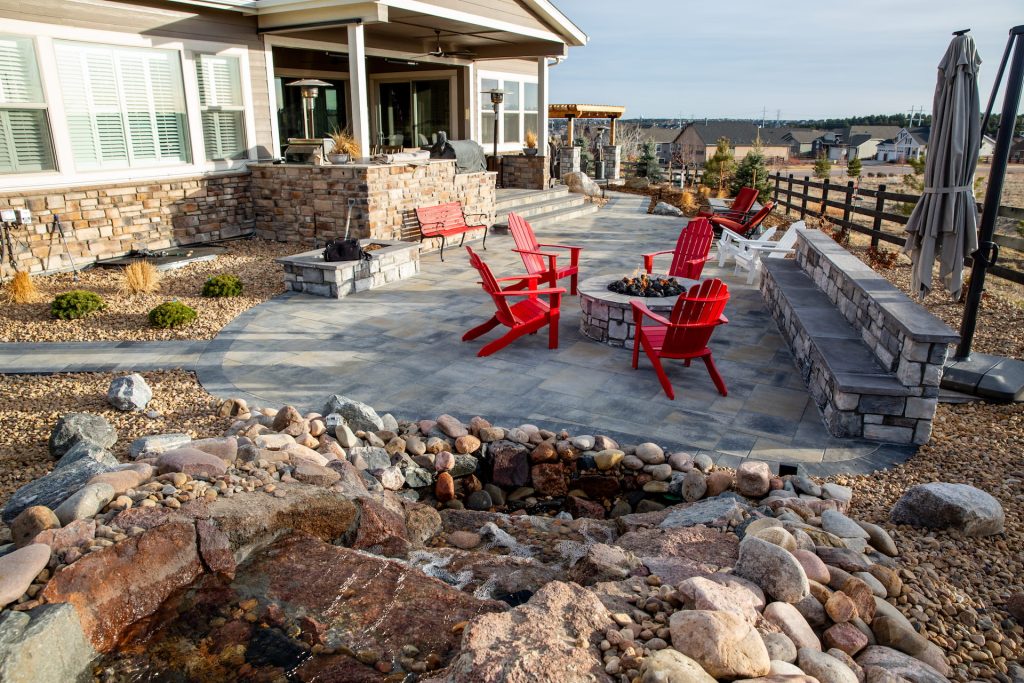 Wide shot of a luxury Belgard paver patio with a built-in fire pit and seating wall in Highlands Ranch.