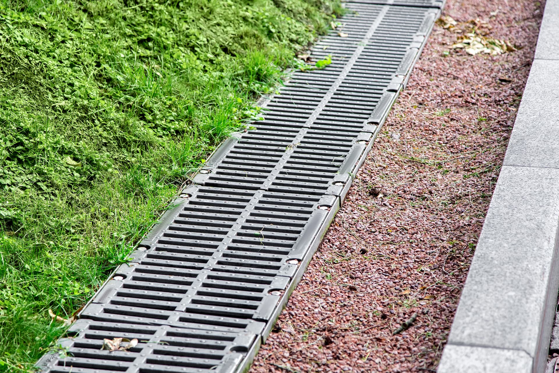 Drainage grate between grass and gravel built by Blue Sky
